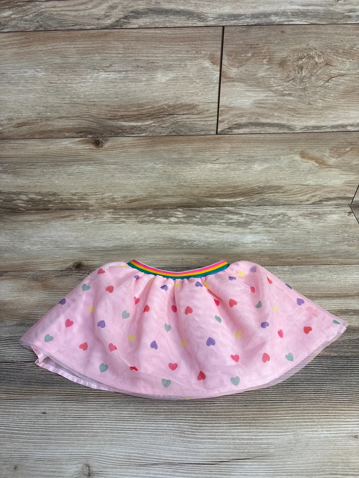 Pink toddler skirt with multicolored heart print and rainbow elastic waistband on wood floor