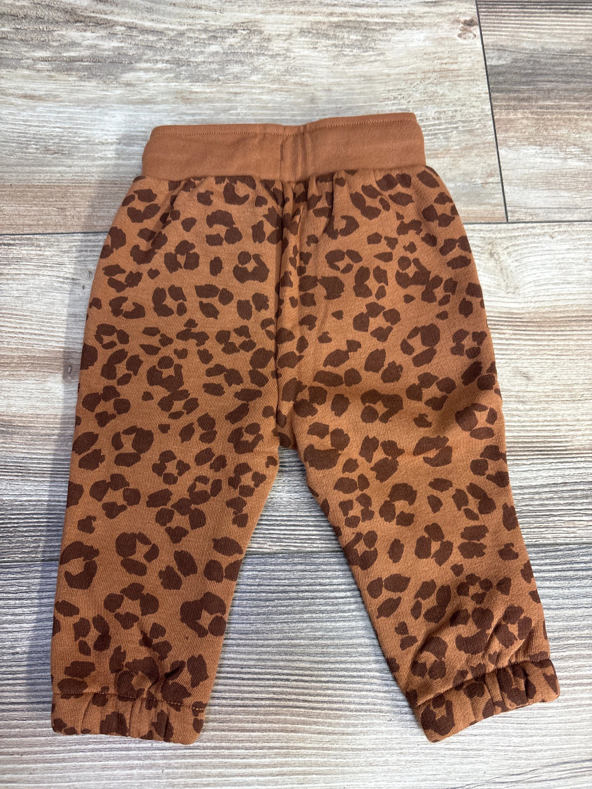 Brown toddler pants with dark brown leopard print and elastic waistband and cuffs on wooden floor