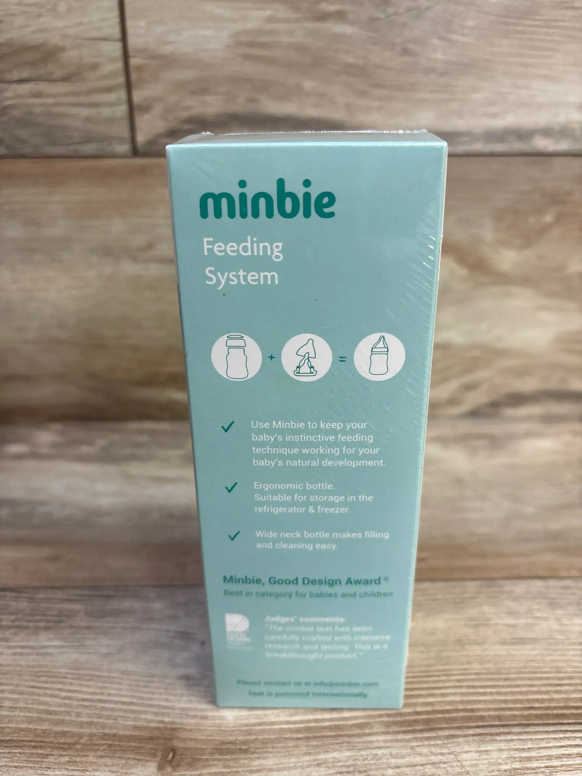 Front view of Minbie 6m+ Feeding Kit box showing 'minbie Feeding System' text, icons and product features on wood surface