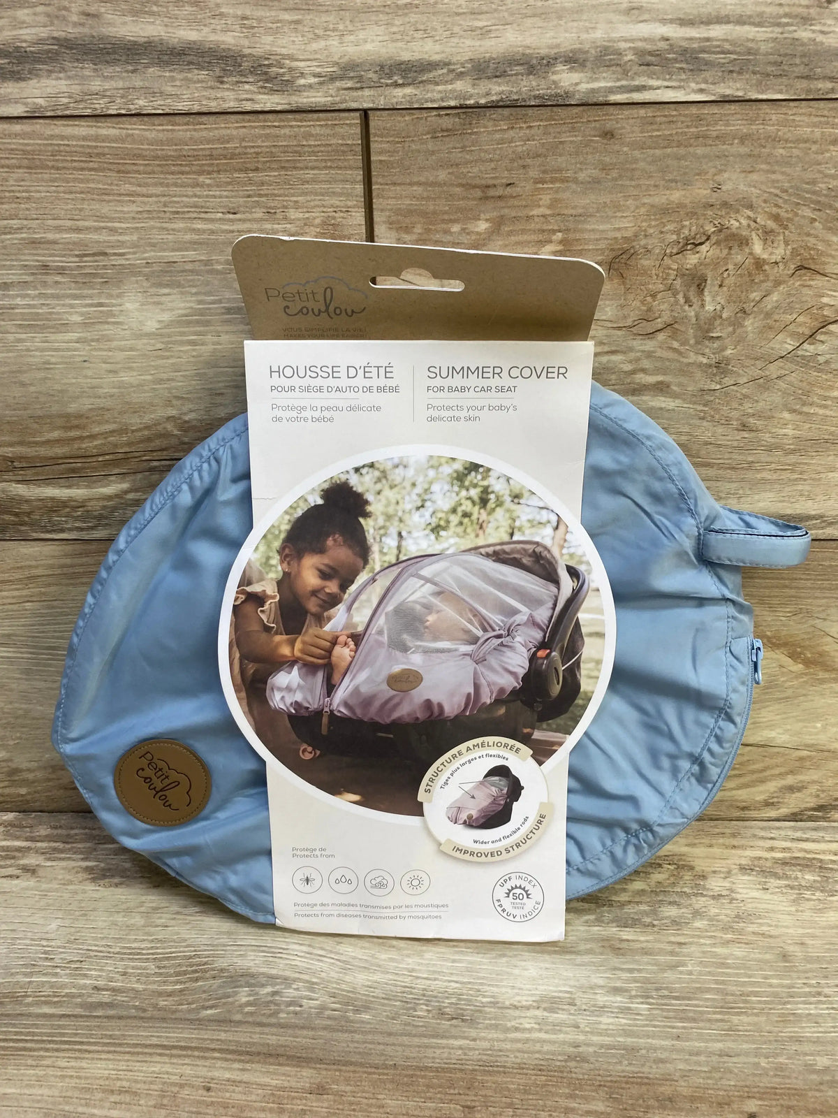 Front view of Petit Coulou summer car seat cover packaging showing blue folded cover and product label on wooden background