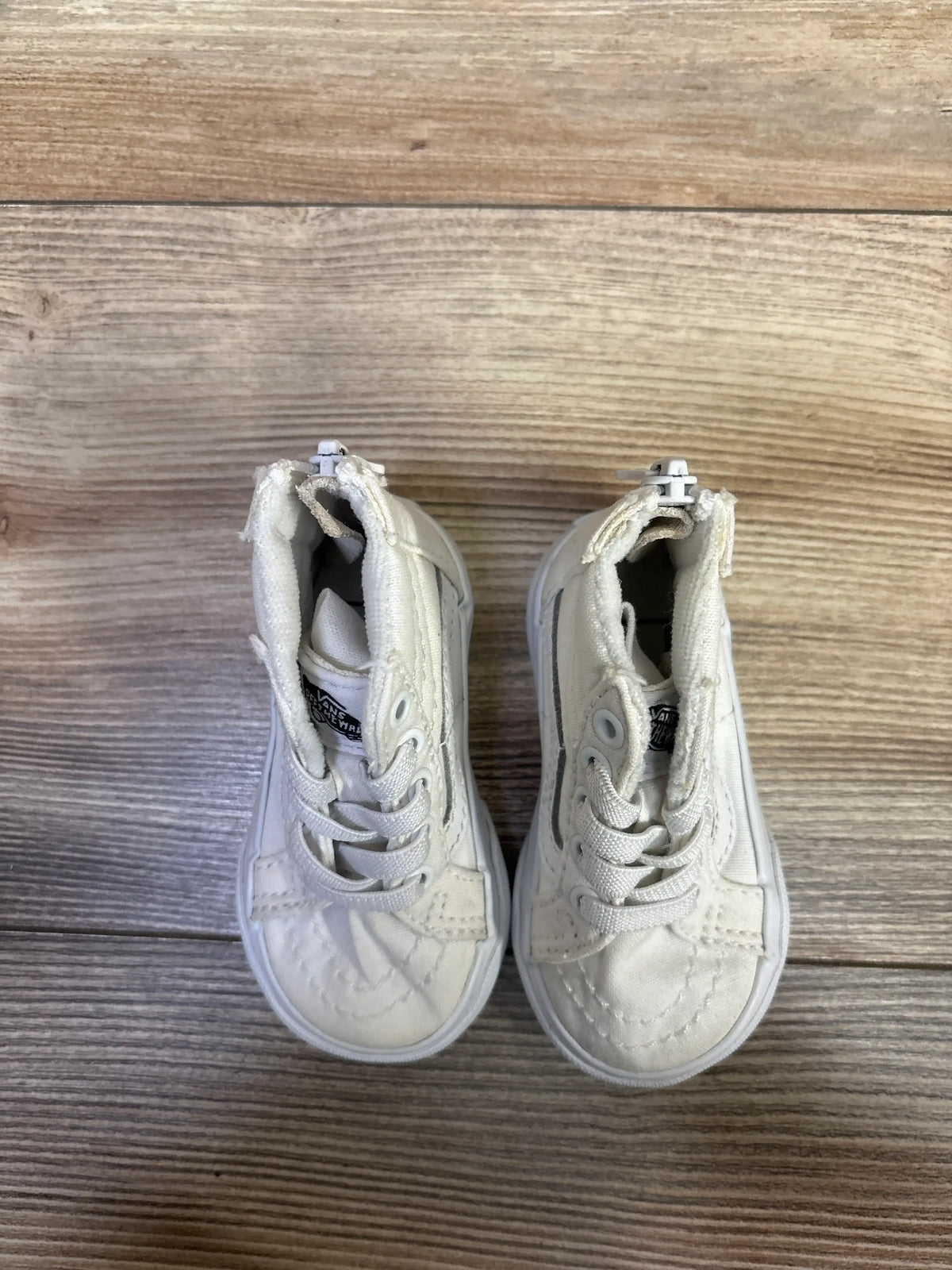 Top view of white Vans Sk8-Hi Zip sneakers in size 3.5C showcasing lace-up fronts and side zippers on a wood-grain background