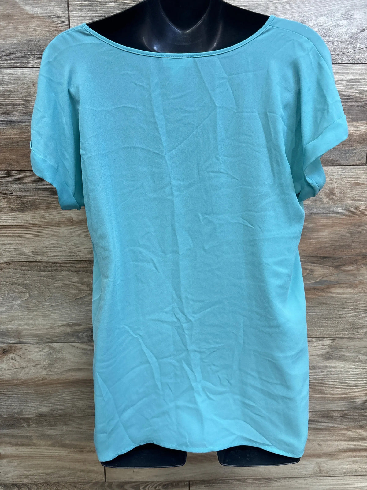 Front view of Motherhood Maternity teal v-neck maternity shirt showcasing its relaxed fit with a wood plank background