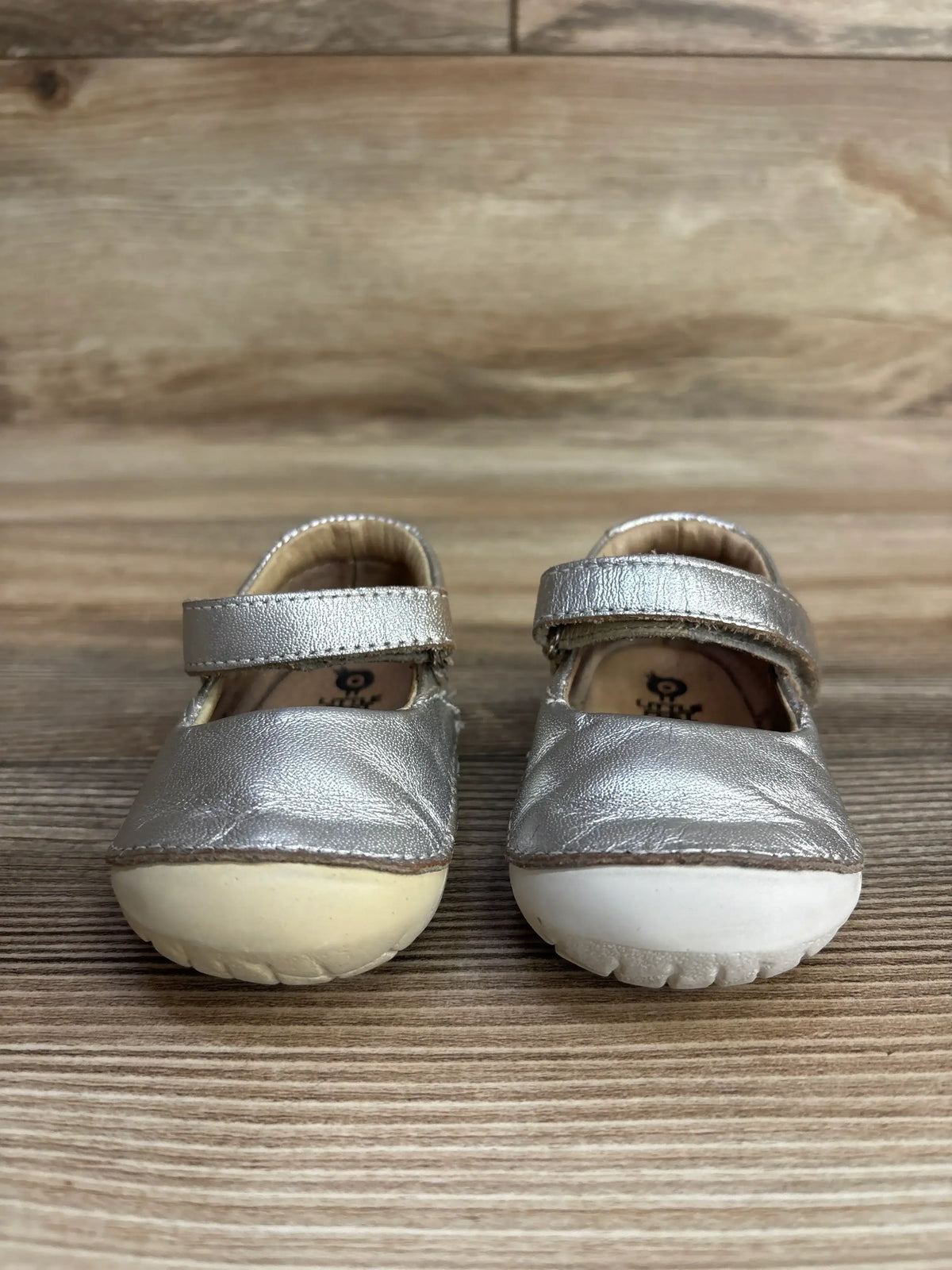 Pair of small metallic silver toddler shoes with velcro straps on wooden floor