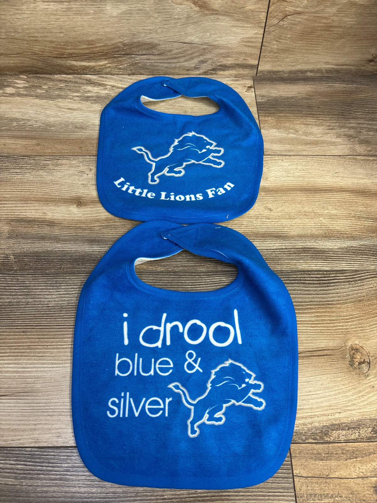 Front view of Detroit Lions drool bibs showcasing Lions graphics and Little Lions Fan and I drool blue and silver text