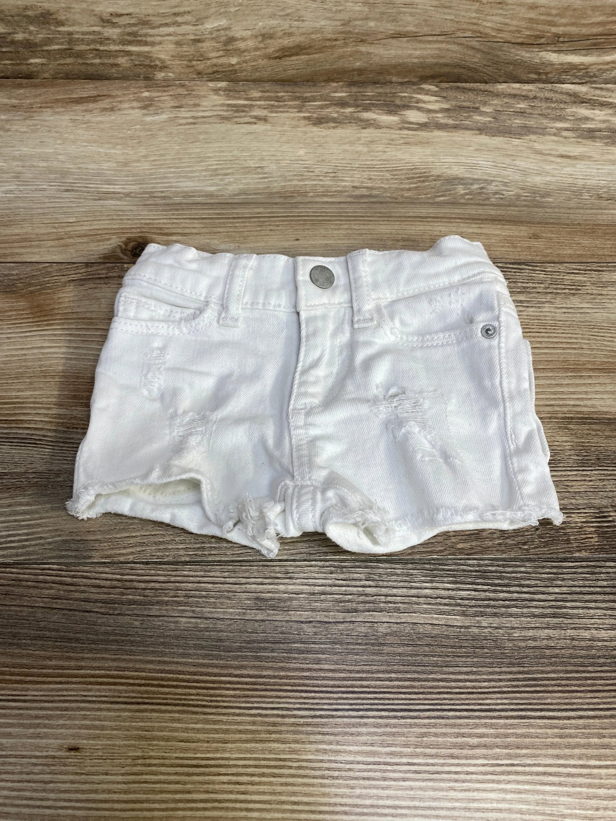 Front view of DL1961 Lucy toddler white denim shorts showing distressed details and frayed hem on wood background