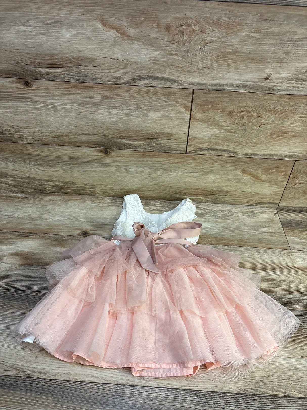 Flat lay of toddler sleeveless dress size 5T with white lace bodice layered blush tulle skirt and satin bow on wood floor