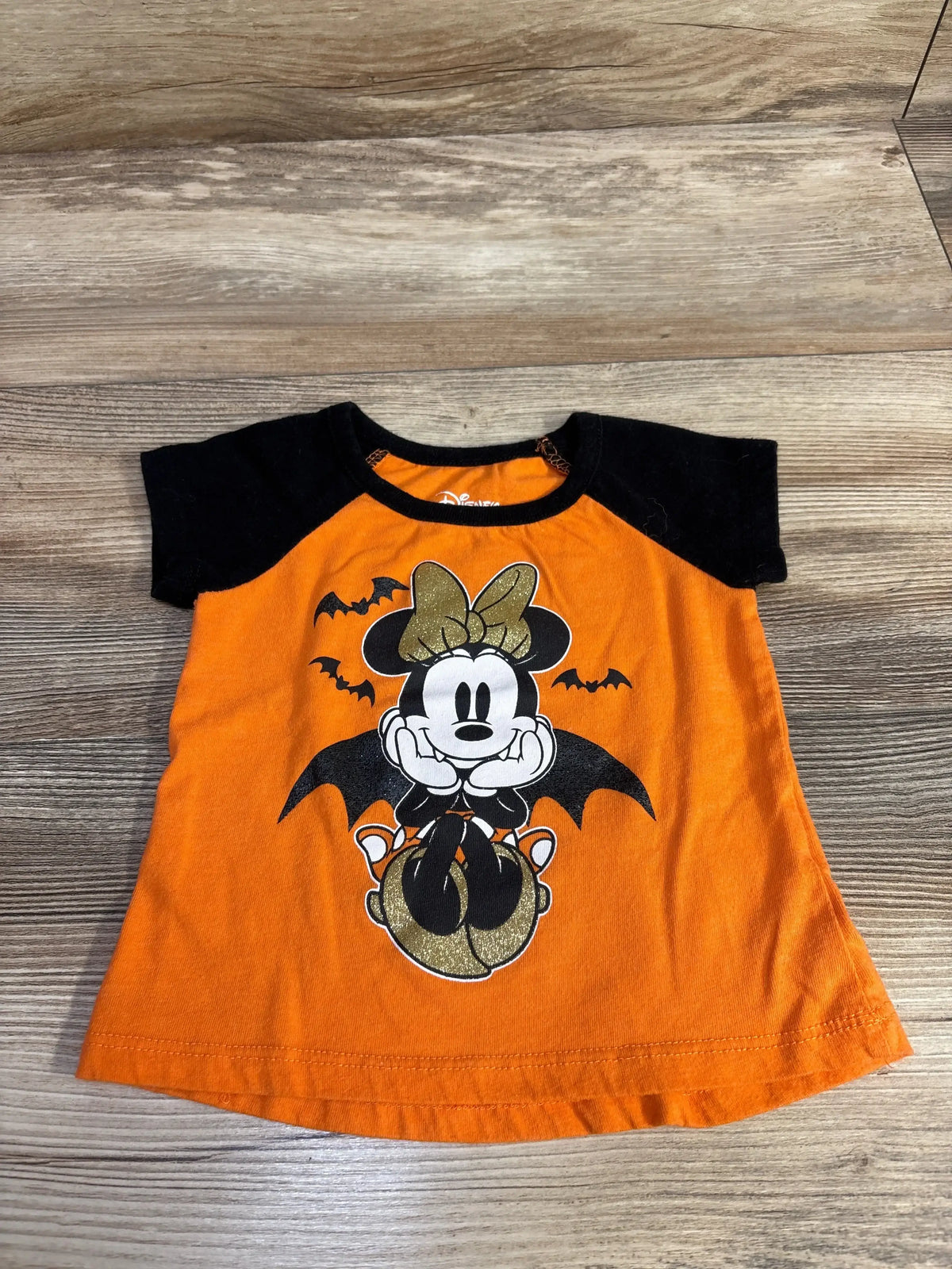 Front view of orange Disney Minnie shirt with black sleeves and Halloween-themed Minnie graphic on a wood floor