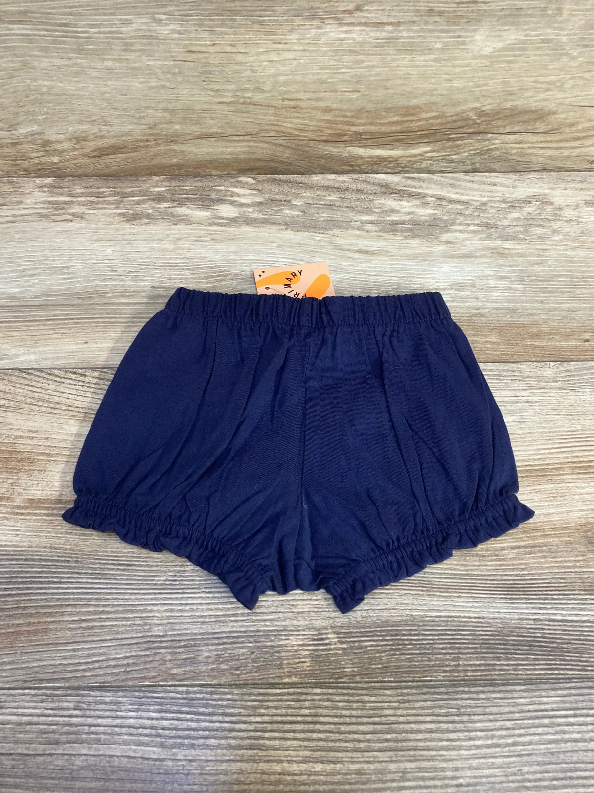 Flat lay of navy baby bloomer showing elastic waistband and ruffled leg openings on light wood background, size 3-6 months