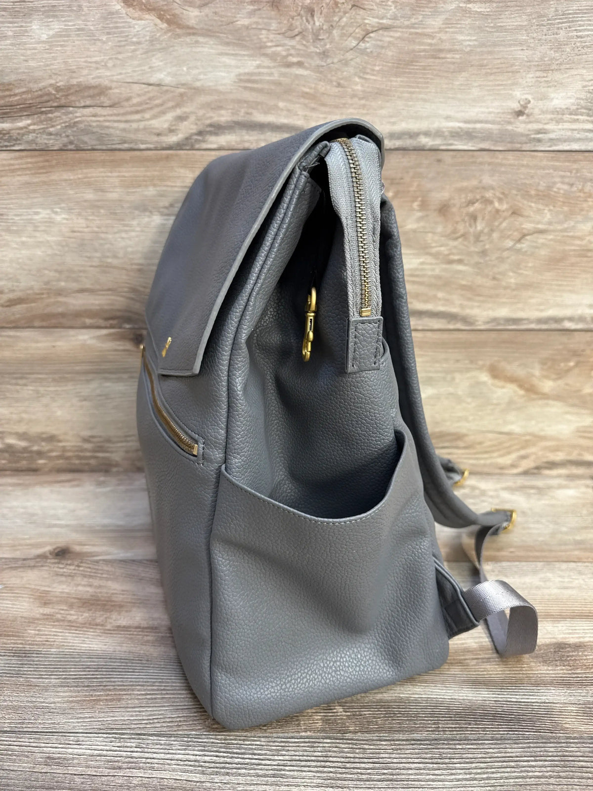 Side view of Freshly Picked Stone Classic Diaper Bag II showing pebbled gray leather, exterior side pocket, and gold hardware on wood background