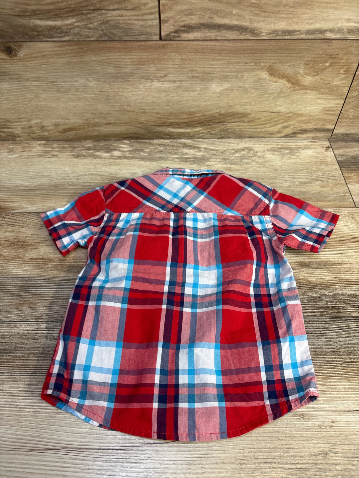 Back view of Faded Gear toddler short-sleeve button-up shirt showing red, blue, and white plaid on wood background