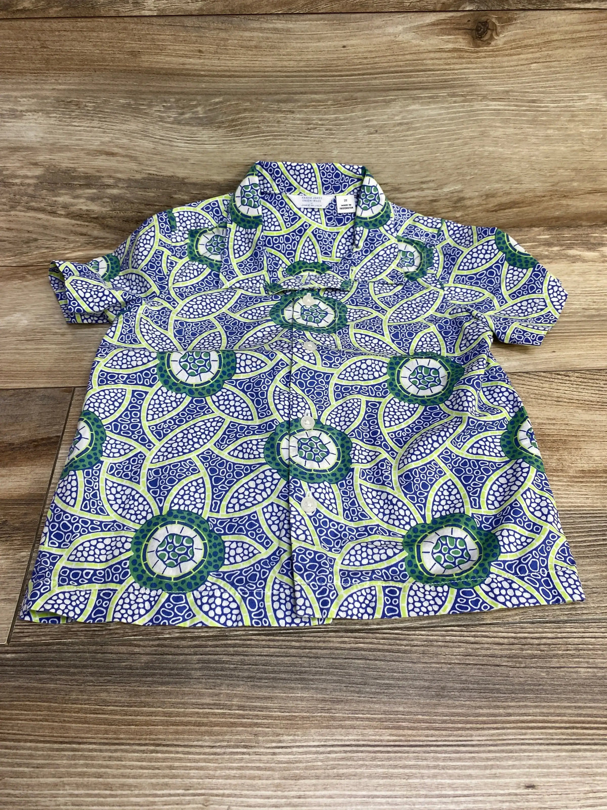 Flat-lay of toddler short-sleeve button-up shirt size 2T showing blue green and white floral print on wood background