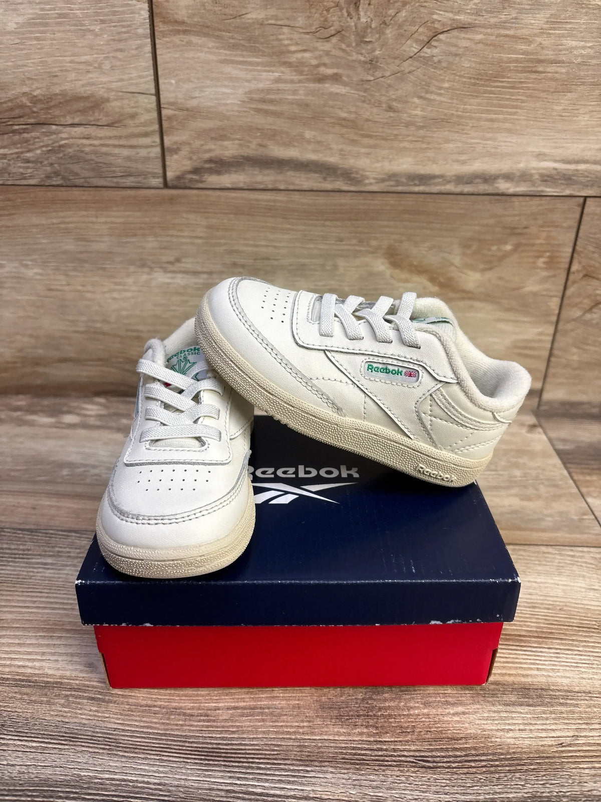 Front and side view of Reebok Club C tennis sneakers in chalk showcasing perforated toes, laces, and Reebok branding on a shoebox