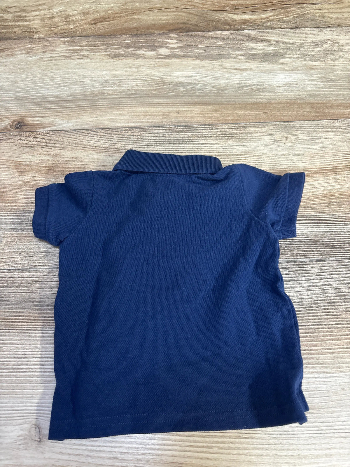 Back view of H&M navy baby polo shirt size 3 months showcasing short sleeves and ribbed collar on light wood background