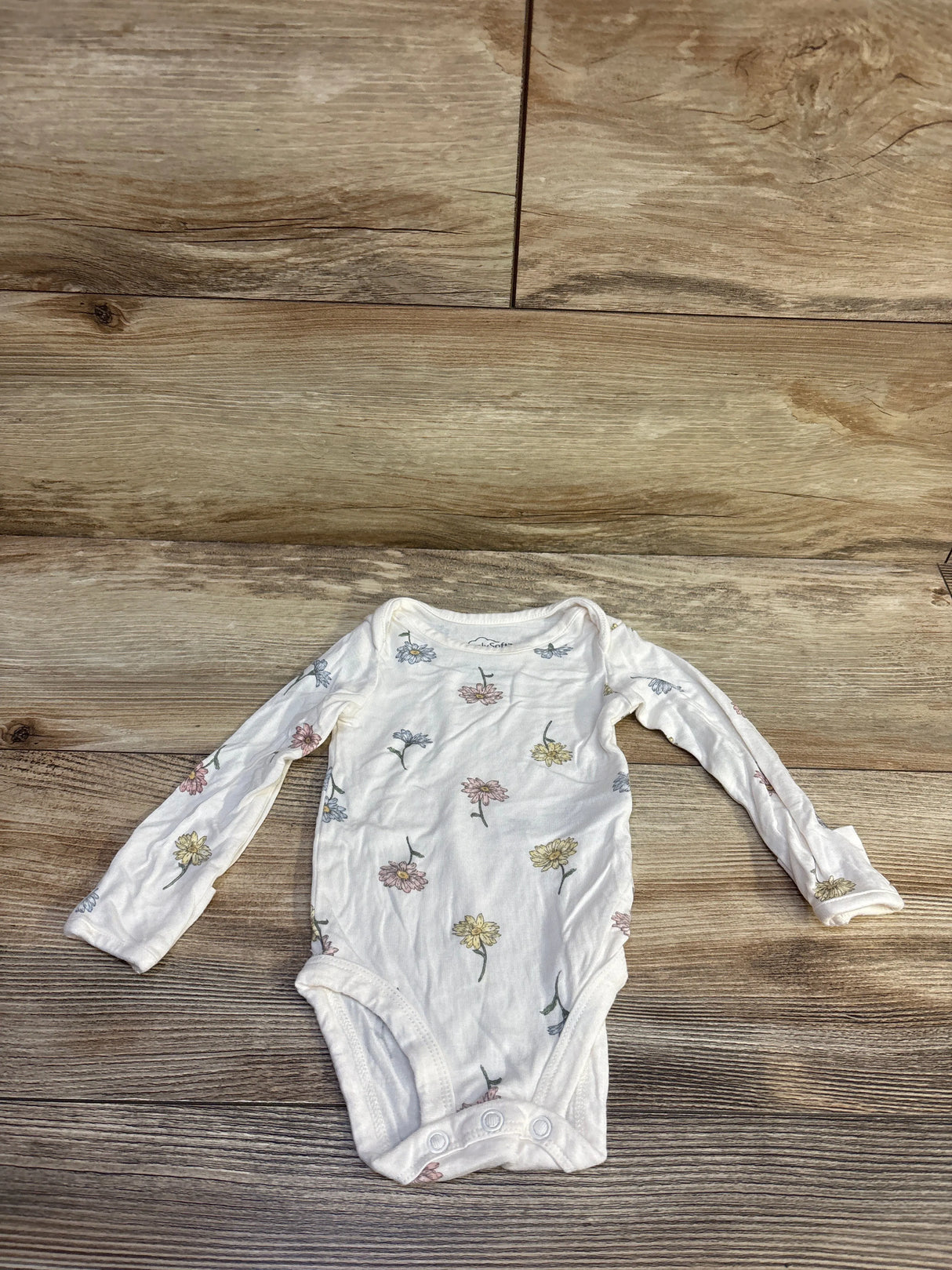 Flat lay of Carter’s PurelySoft long-sleeve baby bodysuit with small floral print and three-snap crotch on wood background