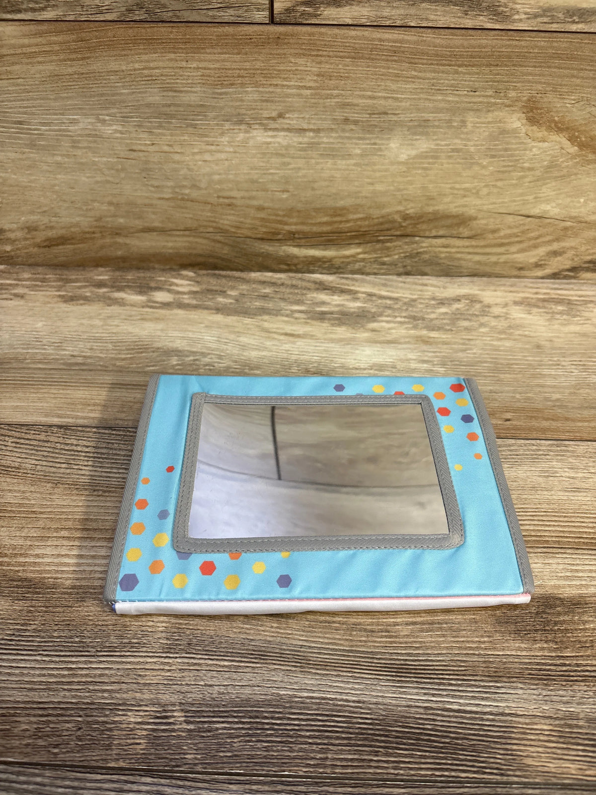 Front view of a prop-up tummy time mirror crinkle high-contrast book with a mirror and colorful hexagon patterns on wood