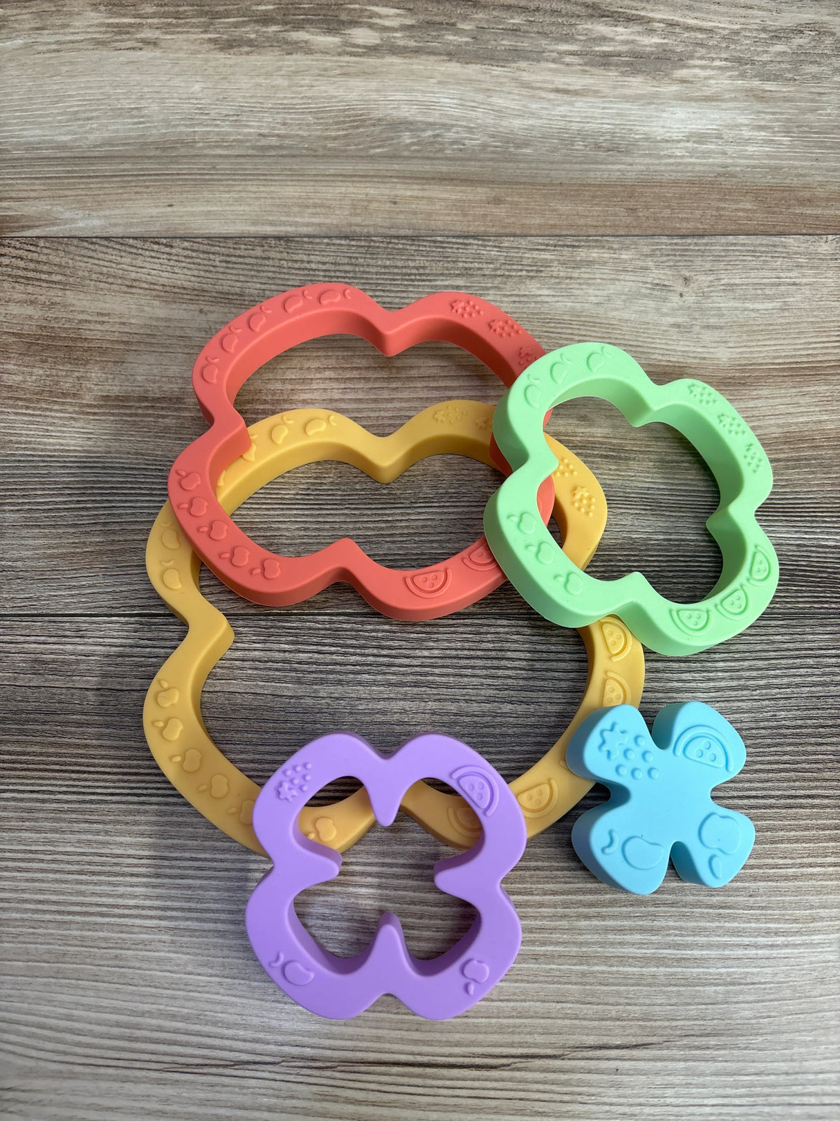 Colorful flower-shaped baby teething rings in red, green, yellow, purple, and blue on a wooden surface