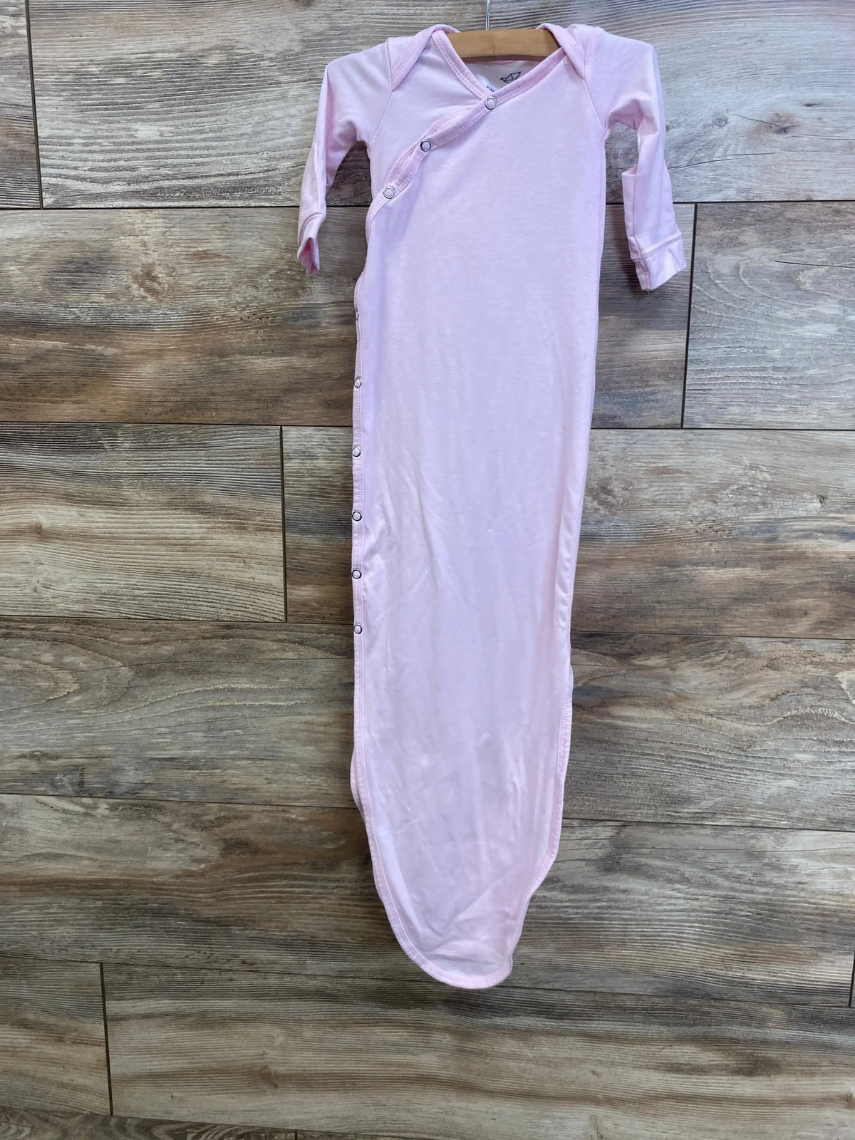 Front view of pink Copper Pearl newborn knotted gown showcasing side snap closures and fold-over cuffs on wood floor