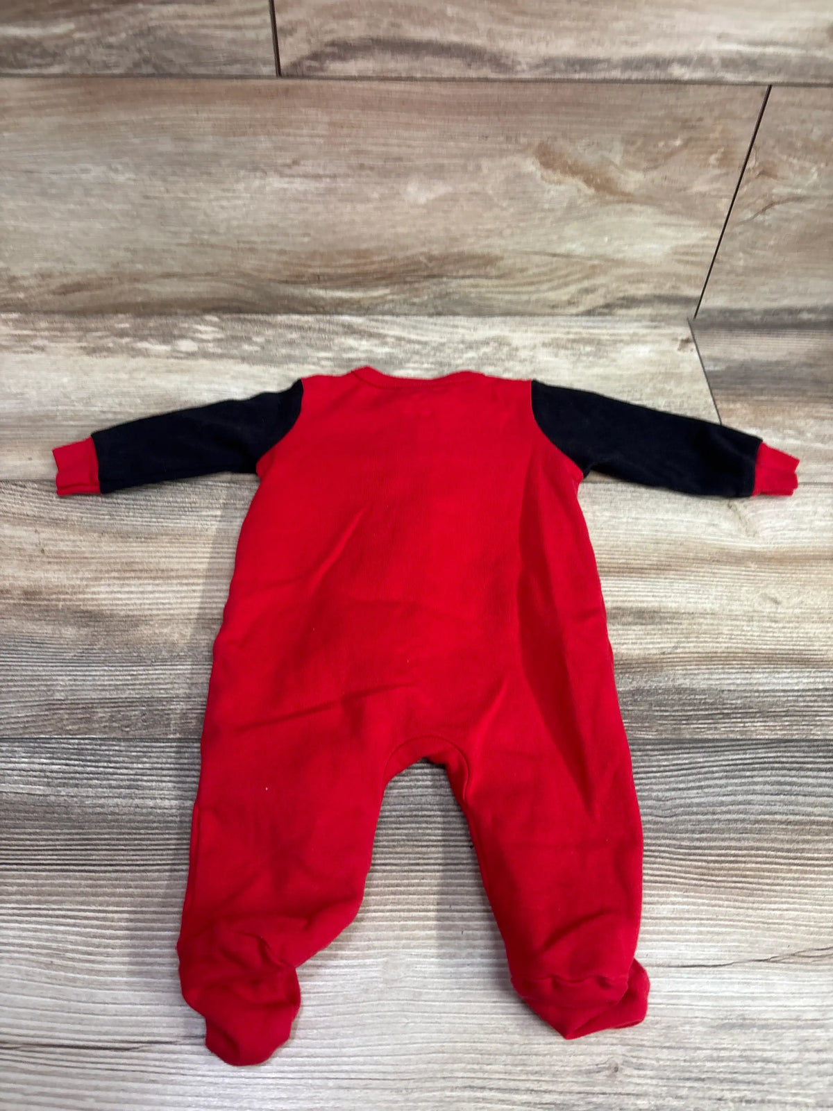 Red baby sleeper with navy blue sleeves laid flat on a wooden surface