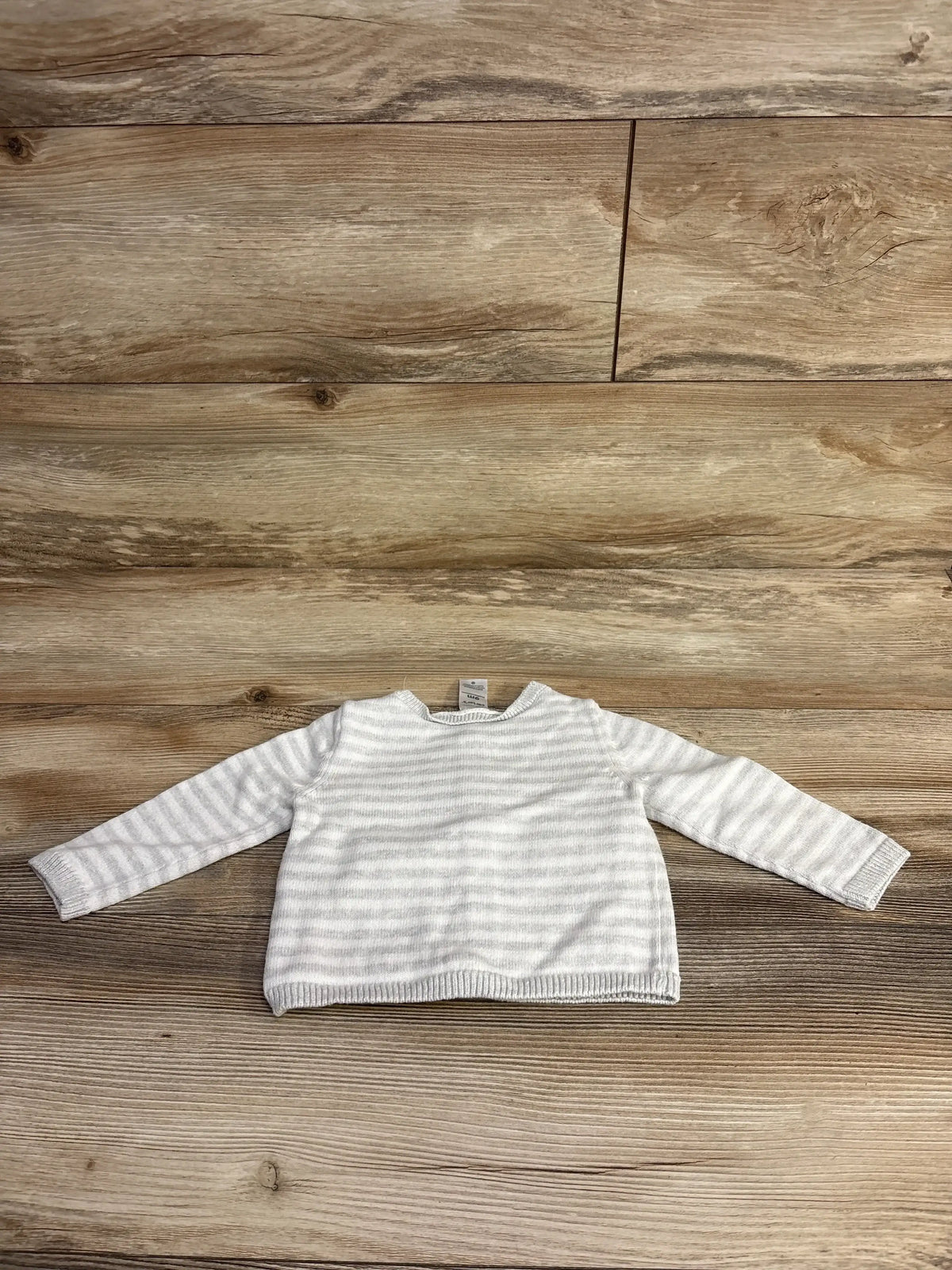 White and light gray striped long-sleeve baby sweater laid flat on wood surface
