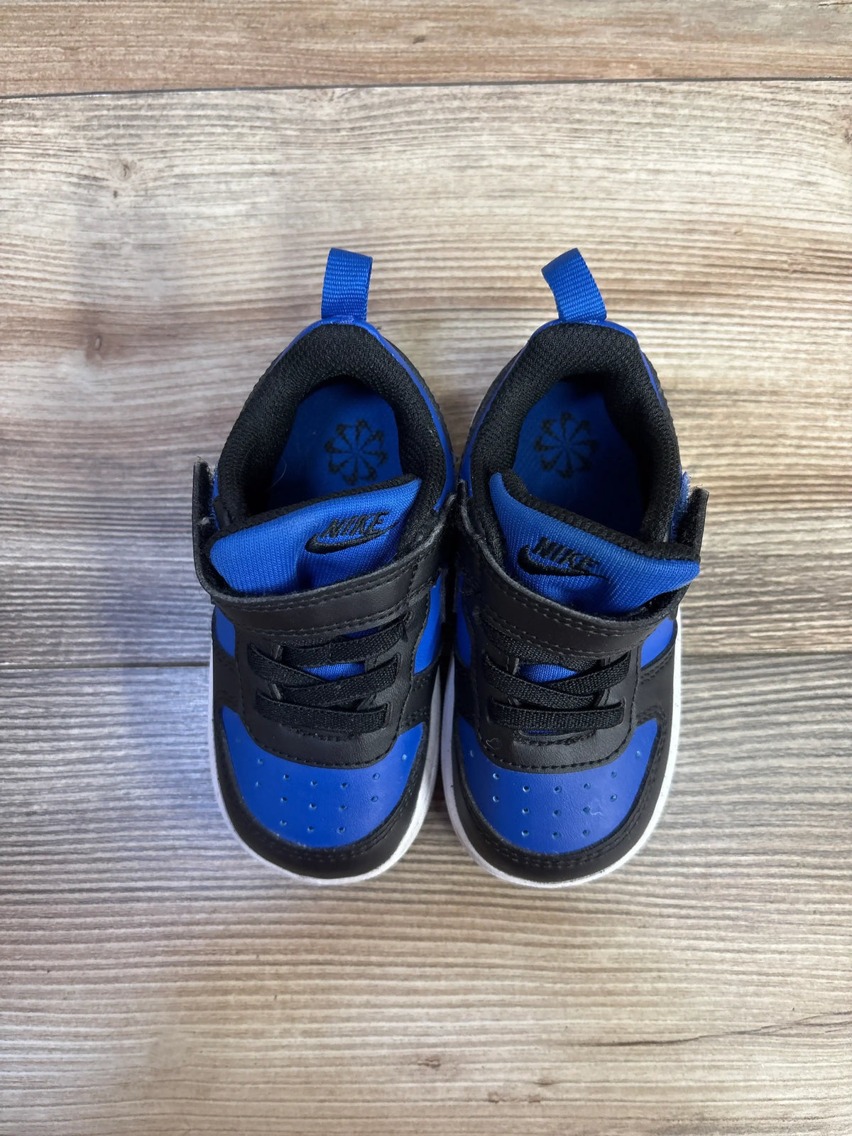 Top view of Nike Court Borough Recraft TD sneakers in Game Royal and Black, showcasing blue and black uppers with wood background
