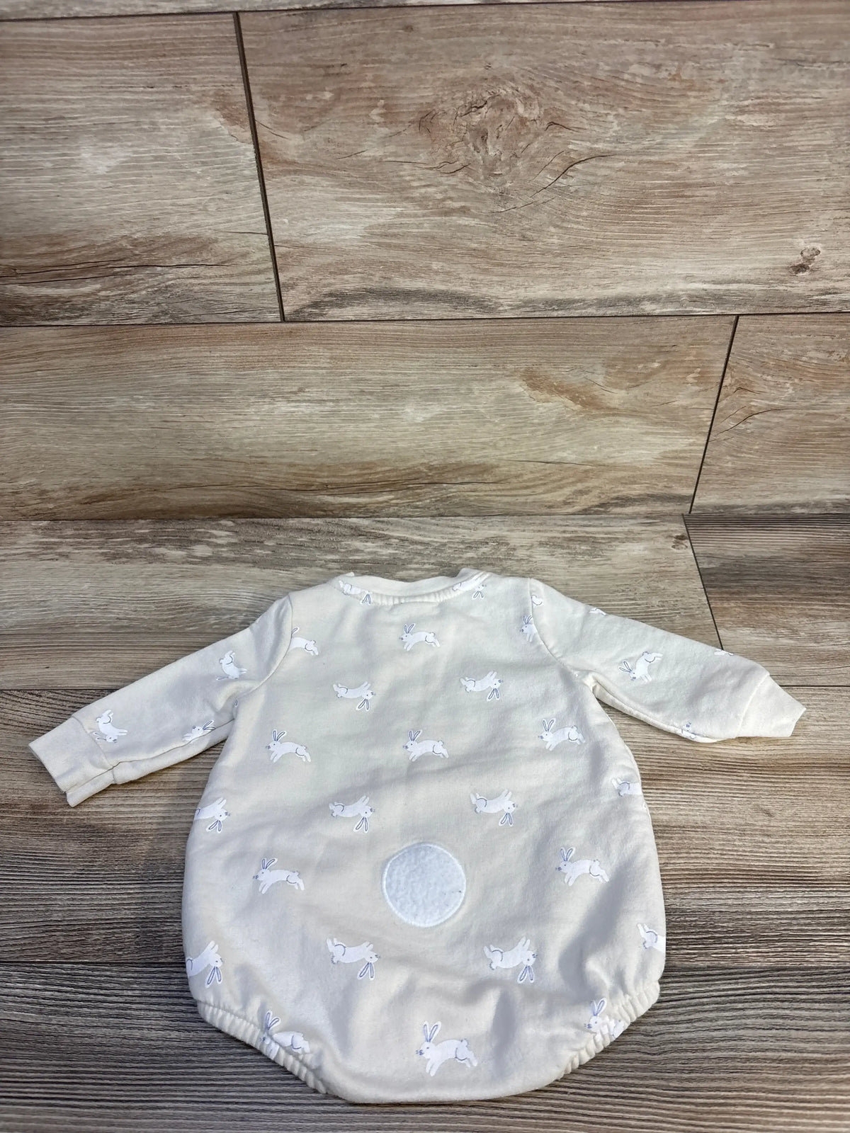 Cream baby sleeper with bunny print and fuzzy patch displayed on wood floor