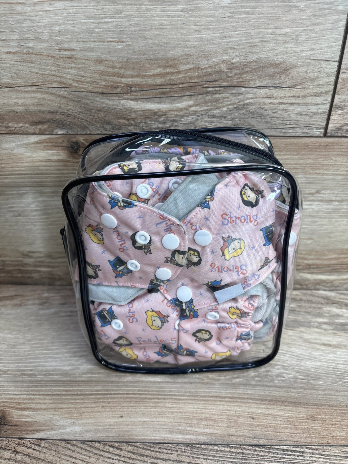 Pink reusable cloth diapers with cartoon print in clear zippered bag on wood background