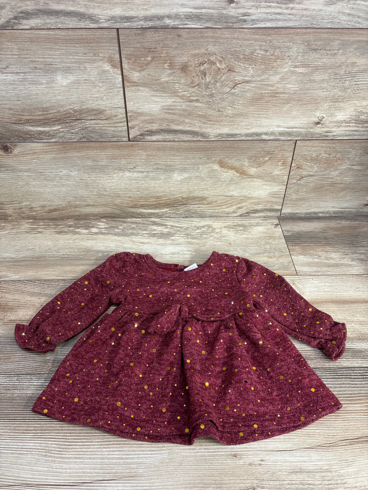 Maroon long-sleeve baby dress with gold polka dots on wood background