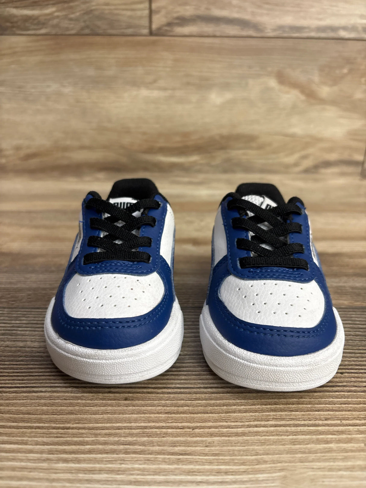 Toddler sneakers with black laces, white and blue leather, on wooden floor