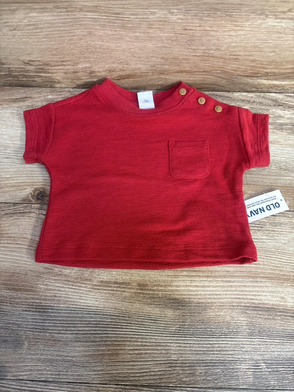 Flat lay of newborn red Old Navy short sleeve shirt showcasing shoulder snap buttons and chest pocket on wood background