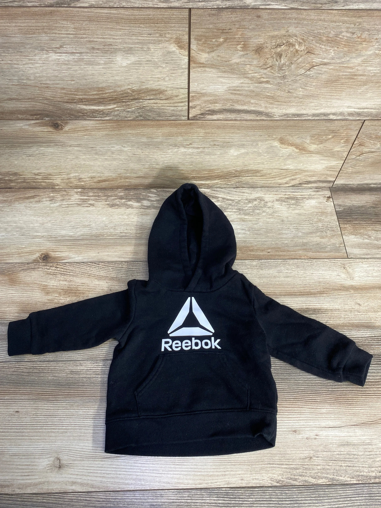 Black Reebok hooded sweatshirt for kids laid flat on wooden floor with front logo