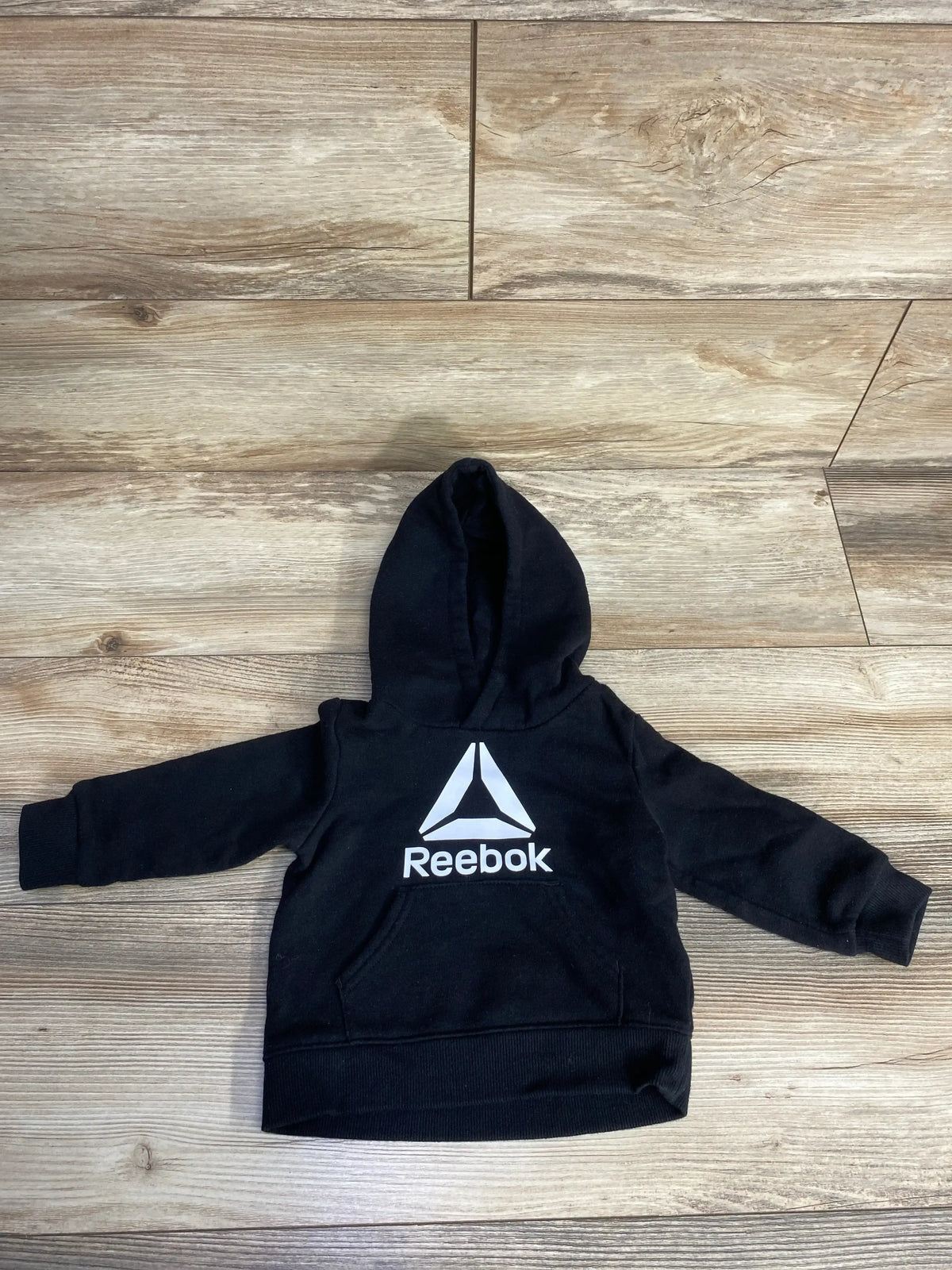 Black Reebok hooded sweatshirt for kids laid flat on wooden floor with front logo