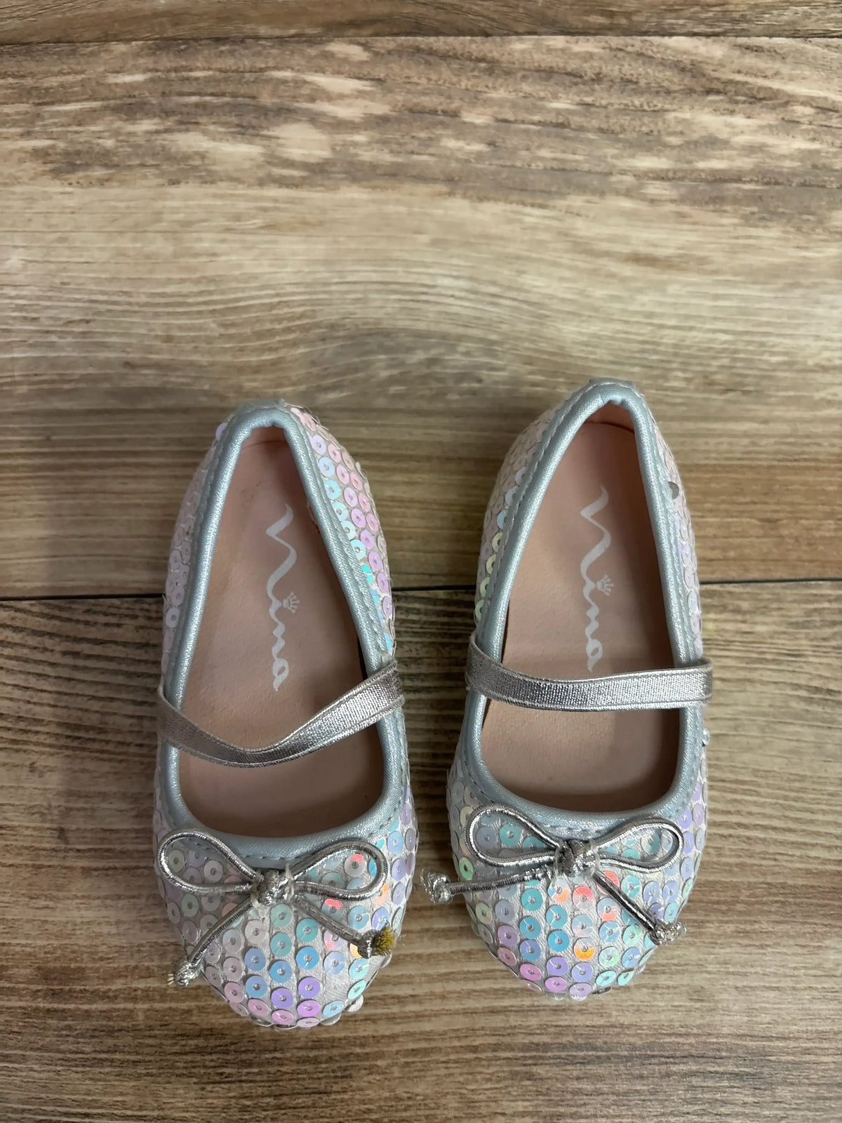 Pair of toddler girls' sequin ballet flats with silver strap and bow on wood floor
