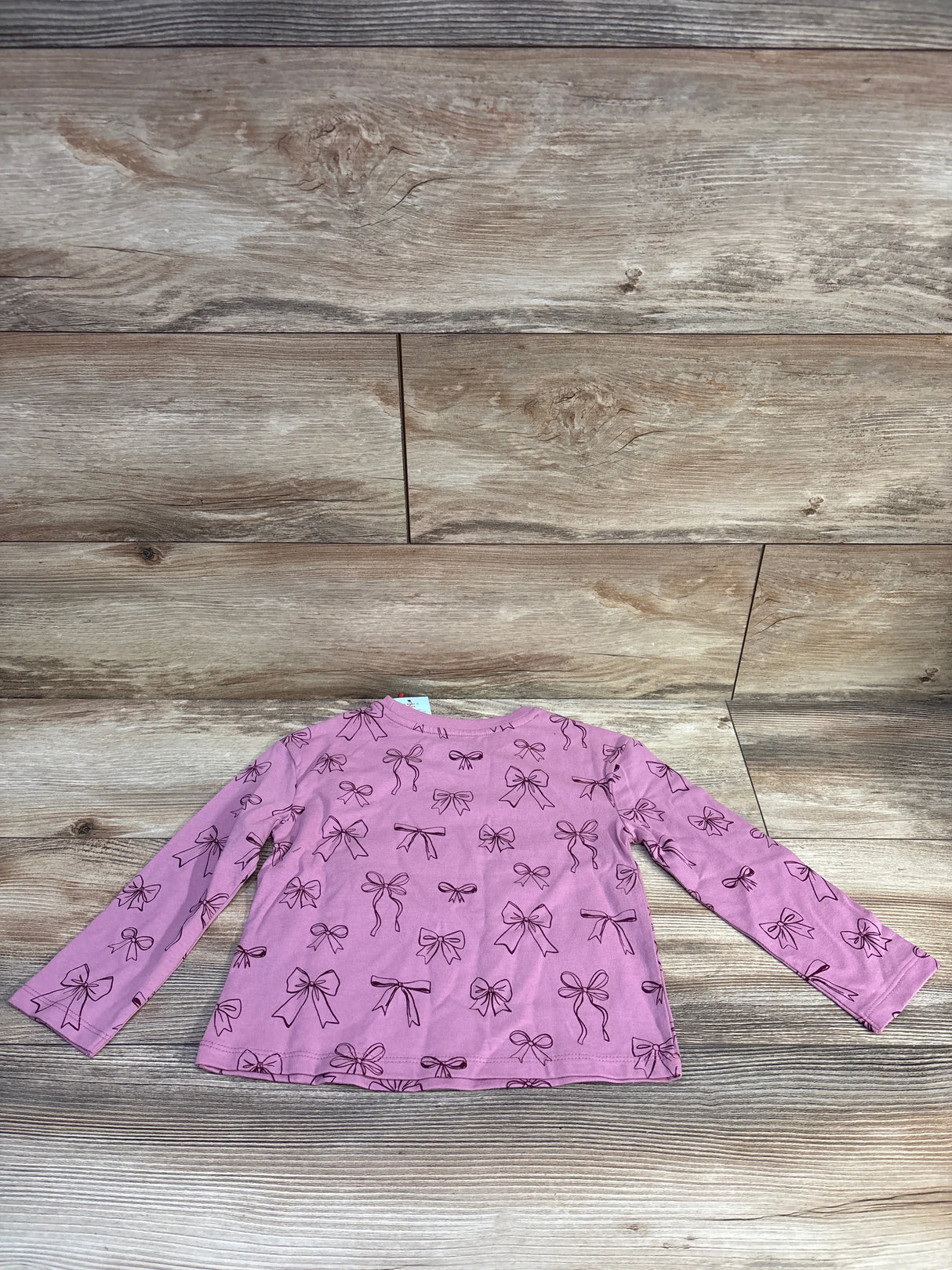 Flat lay of Cat and Jack pink long sleeve toddler shirt size 4T showcasing black bow print on wood background
