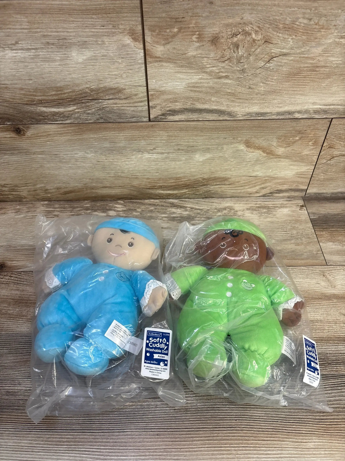 Front view of Lakeshore Cuddly Washable dolls showcasing soft plush fabric and washable tag with dolls sealed in clear plastic on a wood tabletop