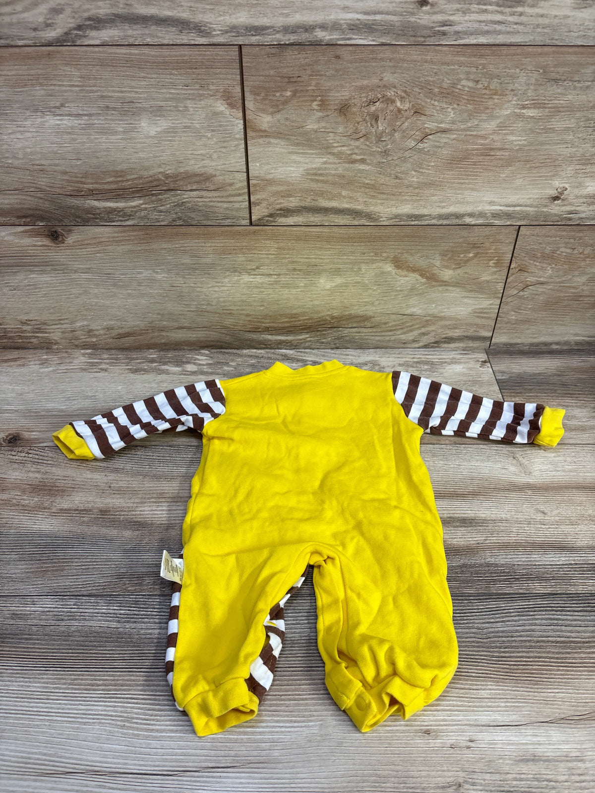 Back view of yellow snap giraffe coverall size 3-6m showing brown and white striped sleeves and leg snaps laid flat on wood floor