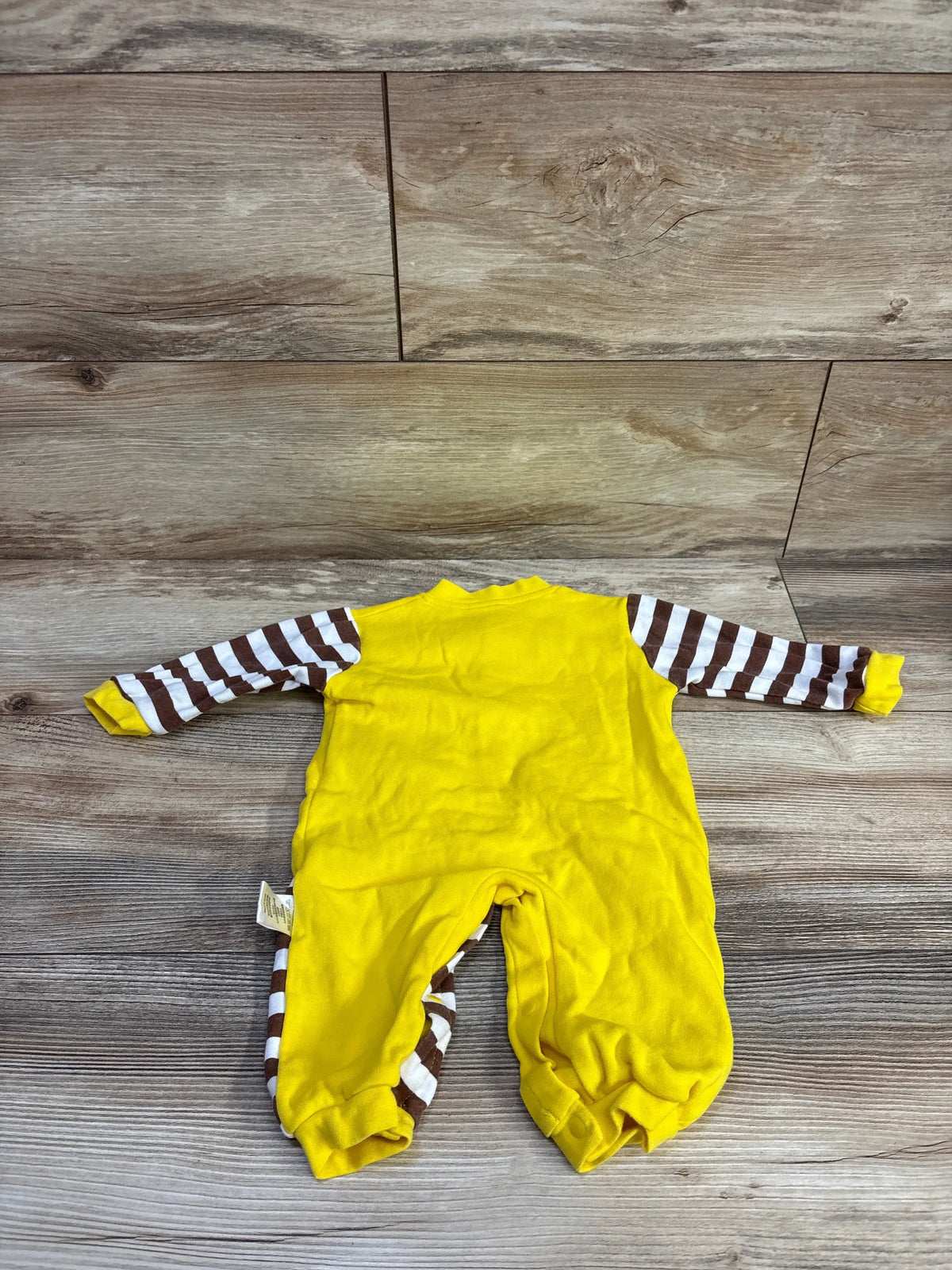 Back view of yellow snap giraffe coverall size 3-6m showing brown and white striped sleeves and leg snaps laid flat on wood floor