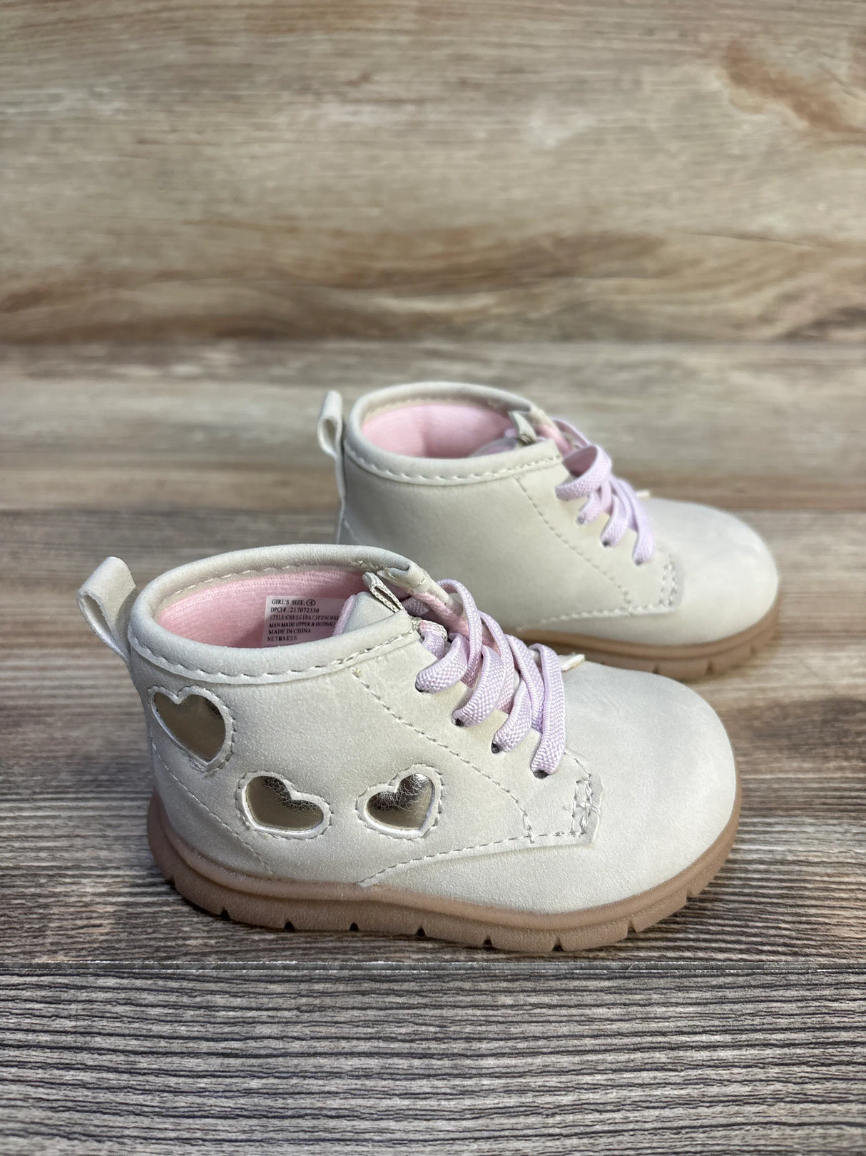 Ivory baby girl boots with pink laces and heart cutouts, toddler footwear on wood background
