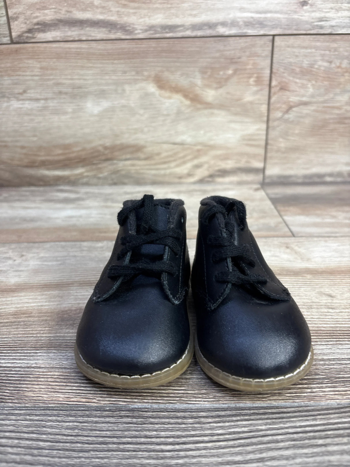Front view of Teeny Toes Oxford baby first-walker shoes in black showing lace-up front and translucent tan sole on wood floor