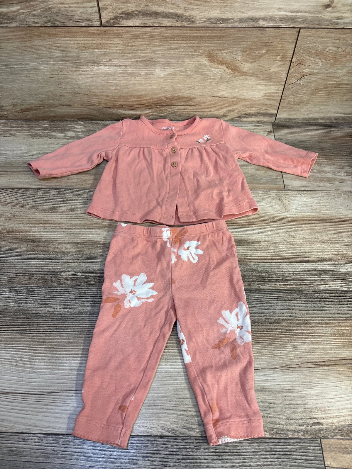 Top view of Carter’s pink two piece button top and bottoms set with floral bottoms on a wood floor