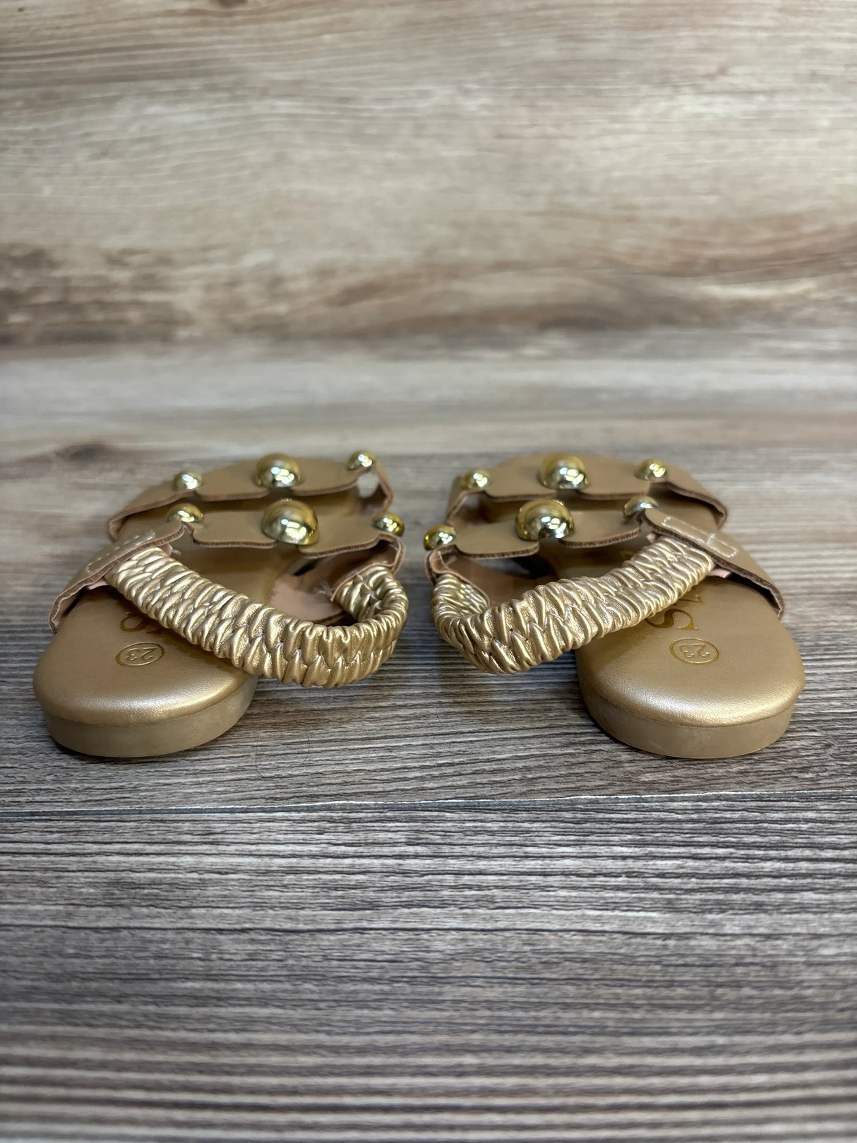 Gold toddler sandals with braided straps and metallic accents on wood floor