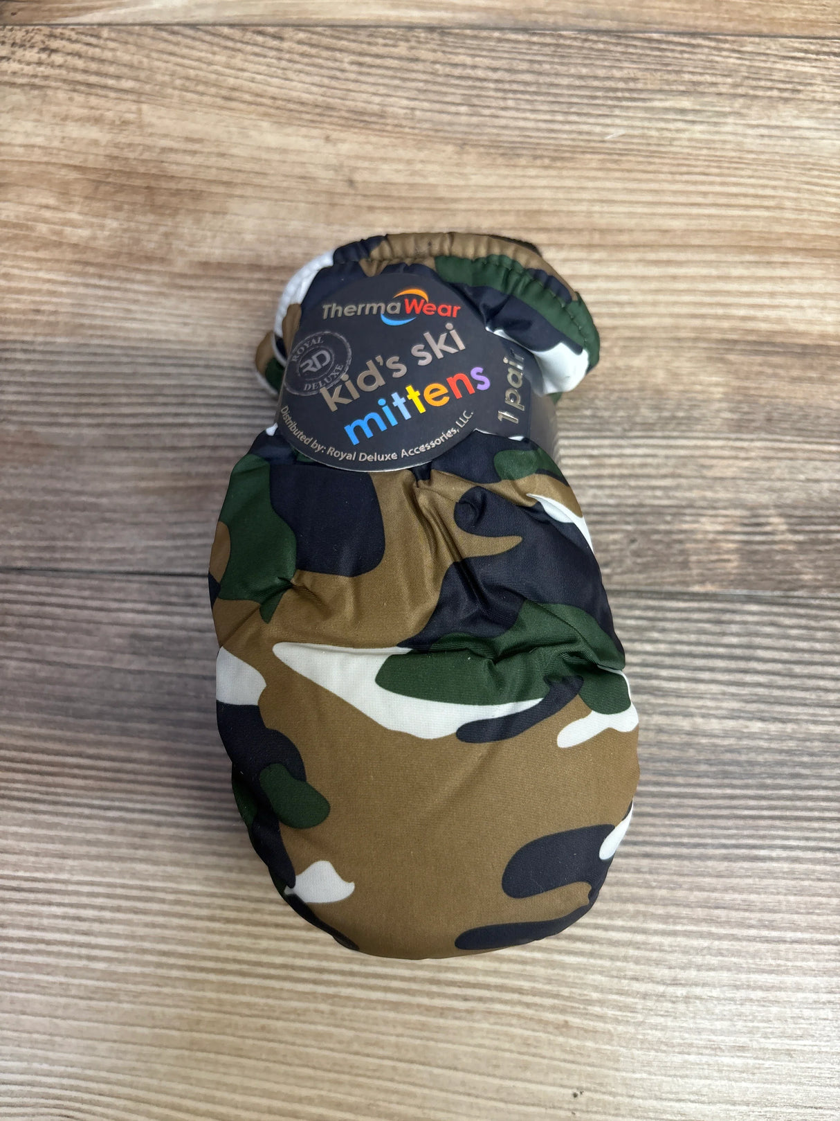 Camouflage patterned kid's ski mittens branded ThermaWear on wooden surface
