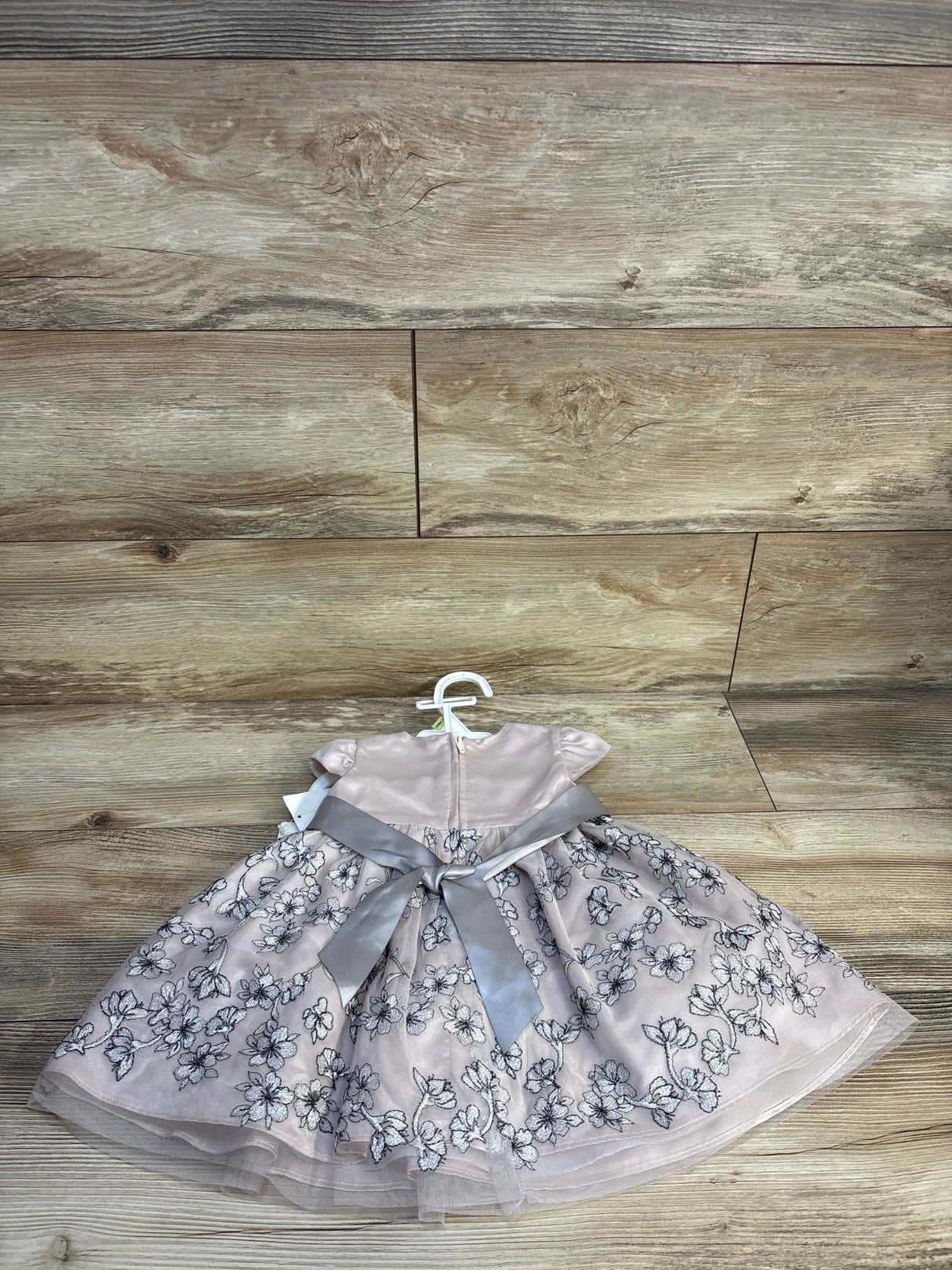 Pink floral baby dress with gray ribbon bow, short sleeves, displayed on wooden background