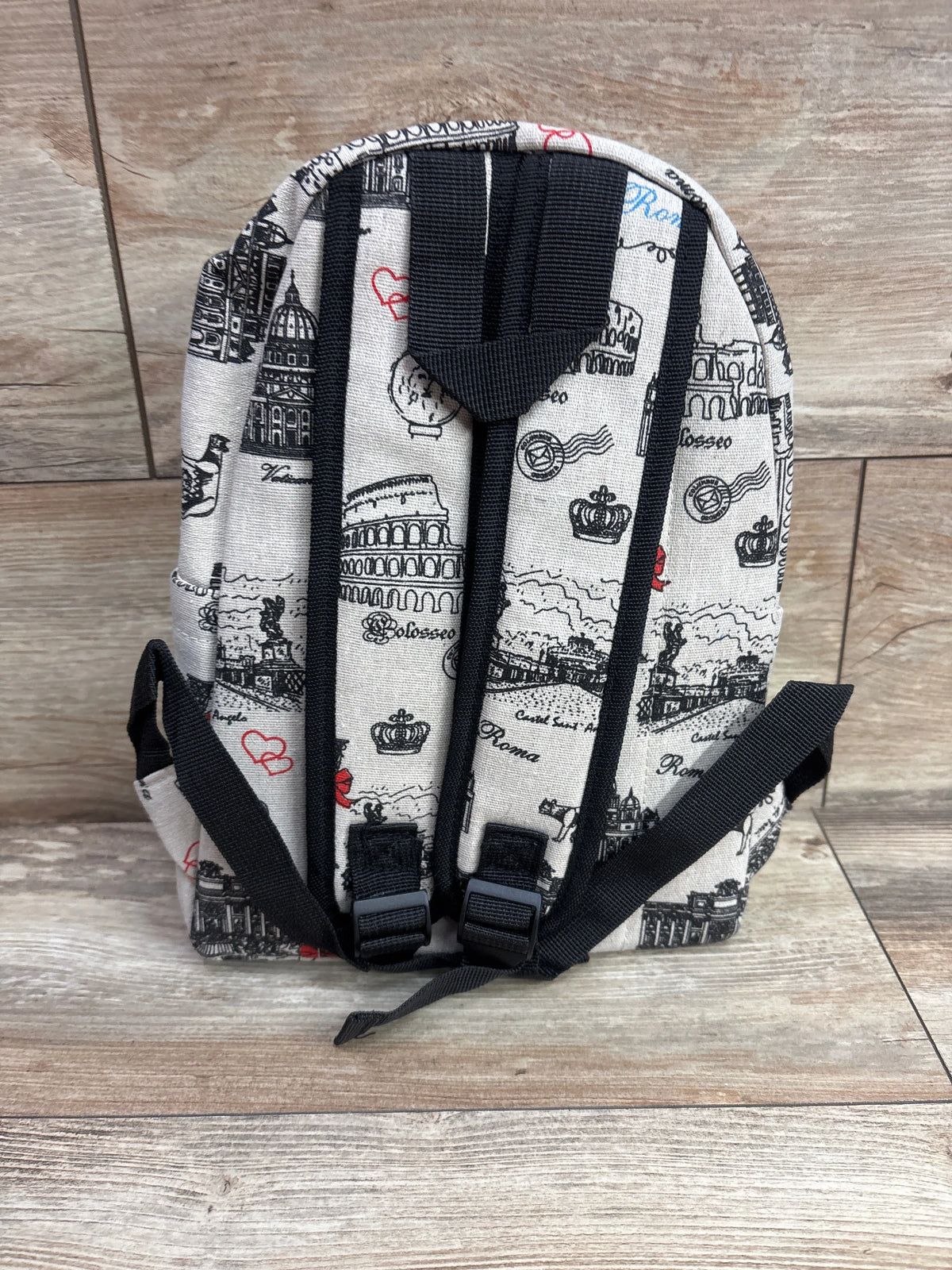 Back view of NWOT Paris mini backpack showcasing cream landmark print and black straps on a wood-look floor