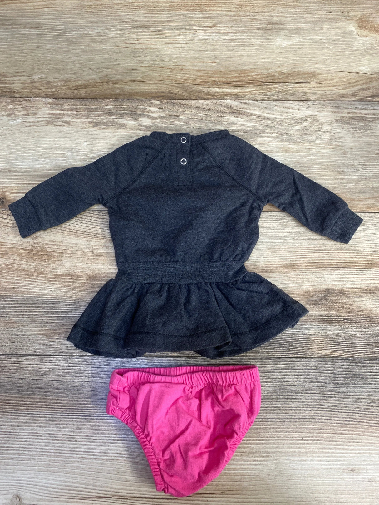 Dark gray baby dress with long sleeves and pink diaper cover on wood background