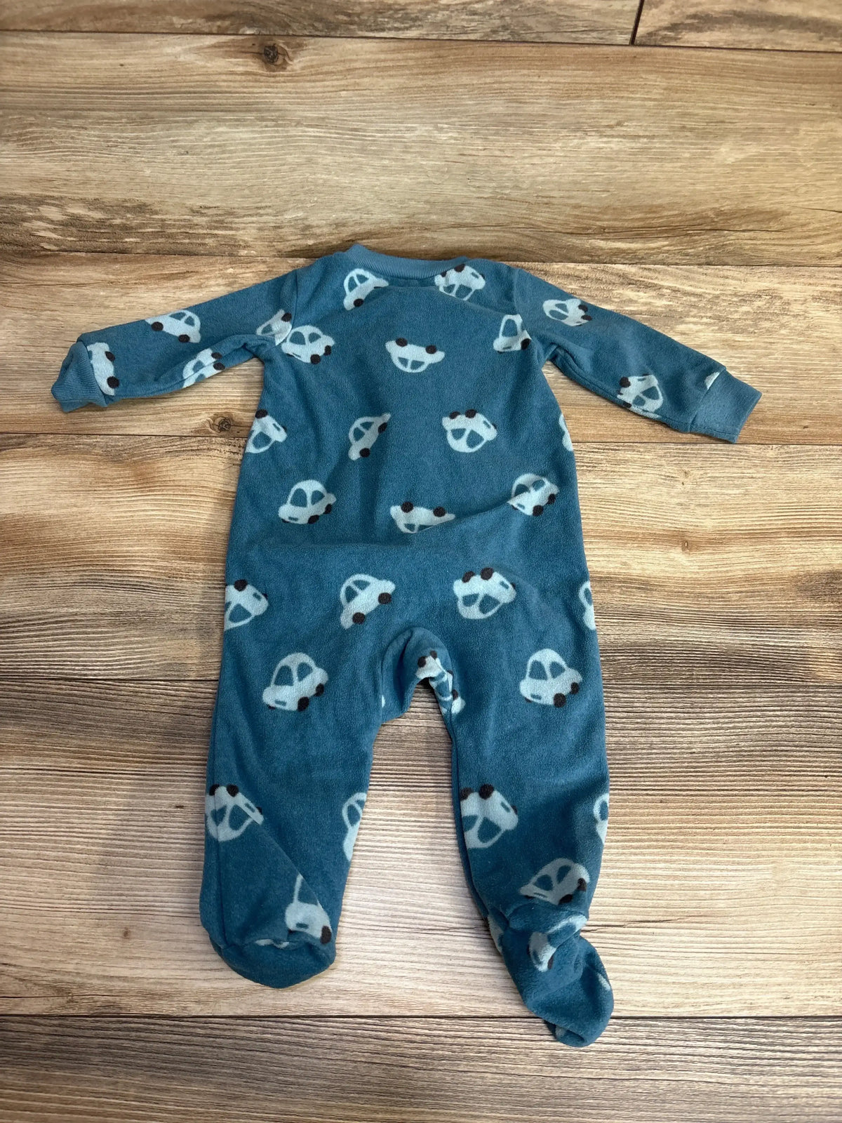 Blue baby footed sleeper with white car print, long sleeves, laid on wooden background