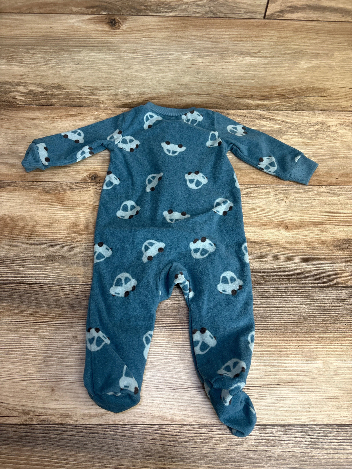 Blue baby footed sleeper with white car print, long sleeves, laid on wooden background