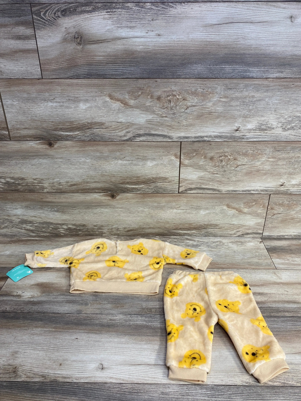Flat lay of NEW Disney Baby Winnie the Pooh 2pc Sweatshirt and Joggers Set in beige with yellow Pooh print and hangtag on a wood plank background