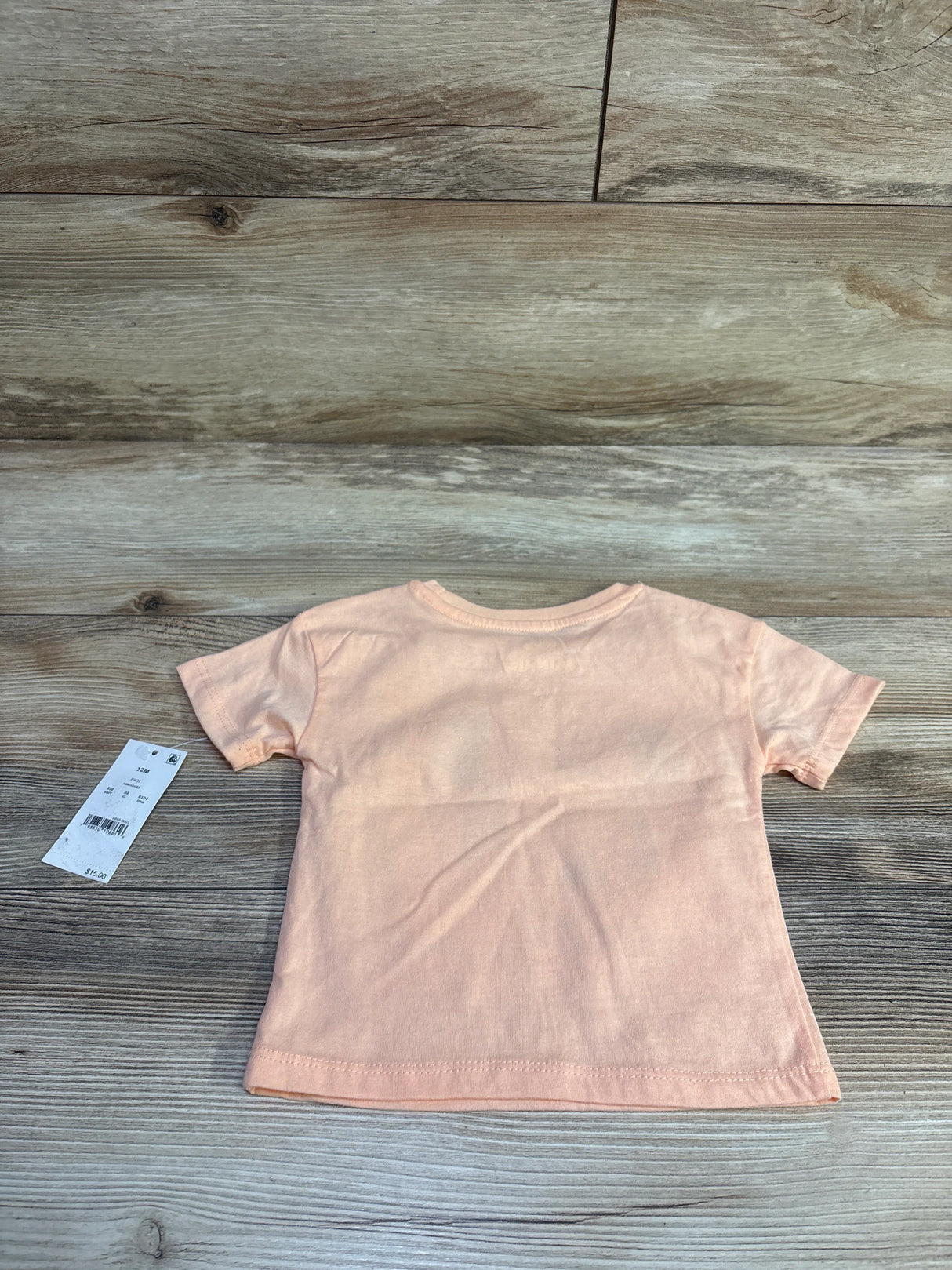 Back view of peach Disney Minnie Mouse toddler tee with retail tag on light wood background