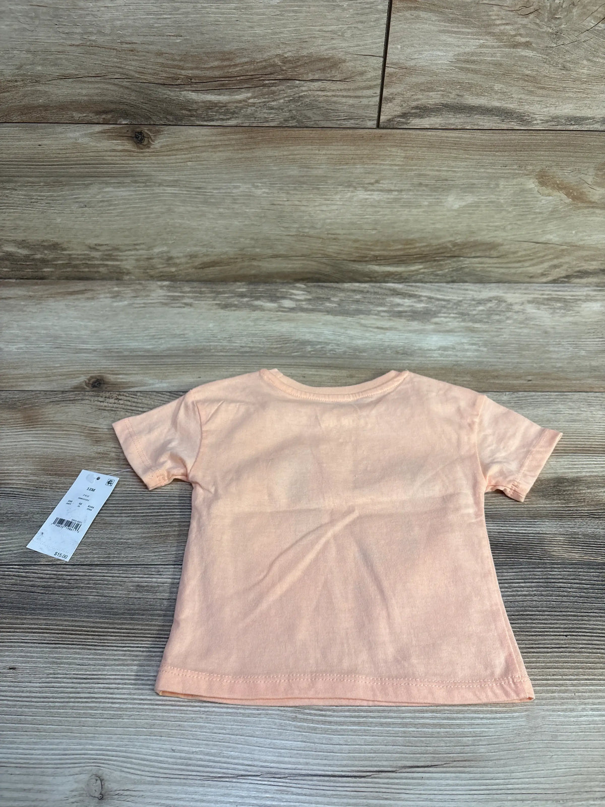Back view of peach Disney Minnie Mouse toddler tee with retail tag on light wood background