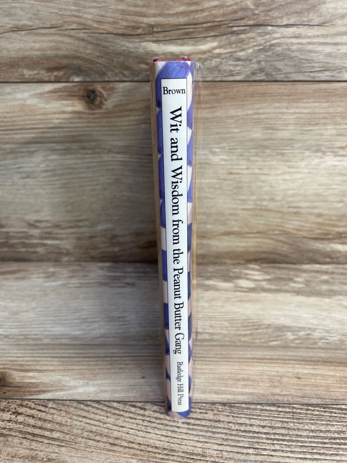 Spine view of Wit and Wisdom from the Peanut Butter Gang hardcover showcasing title and purple patterned dust jacket on wood background
